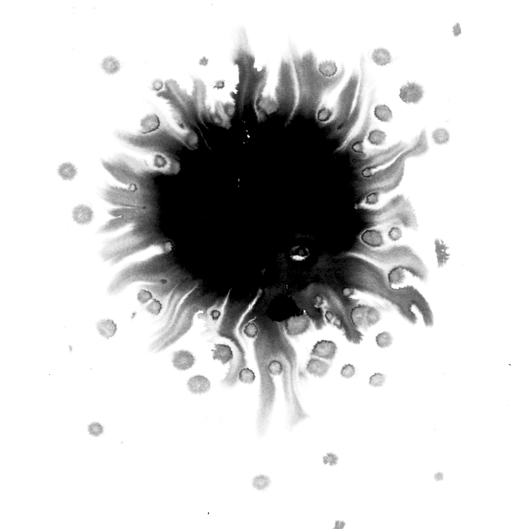 Ink blob on wet paper with radial flame-like spikes and scattered satellite droplets surrounding a dense black center